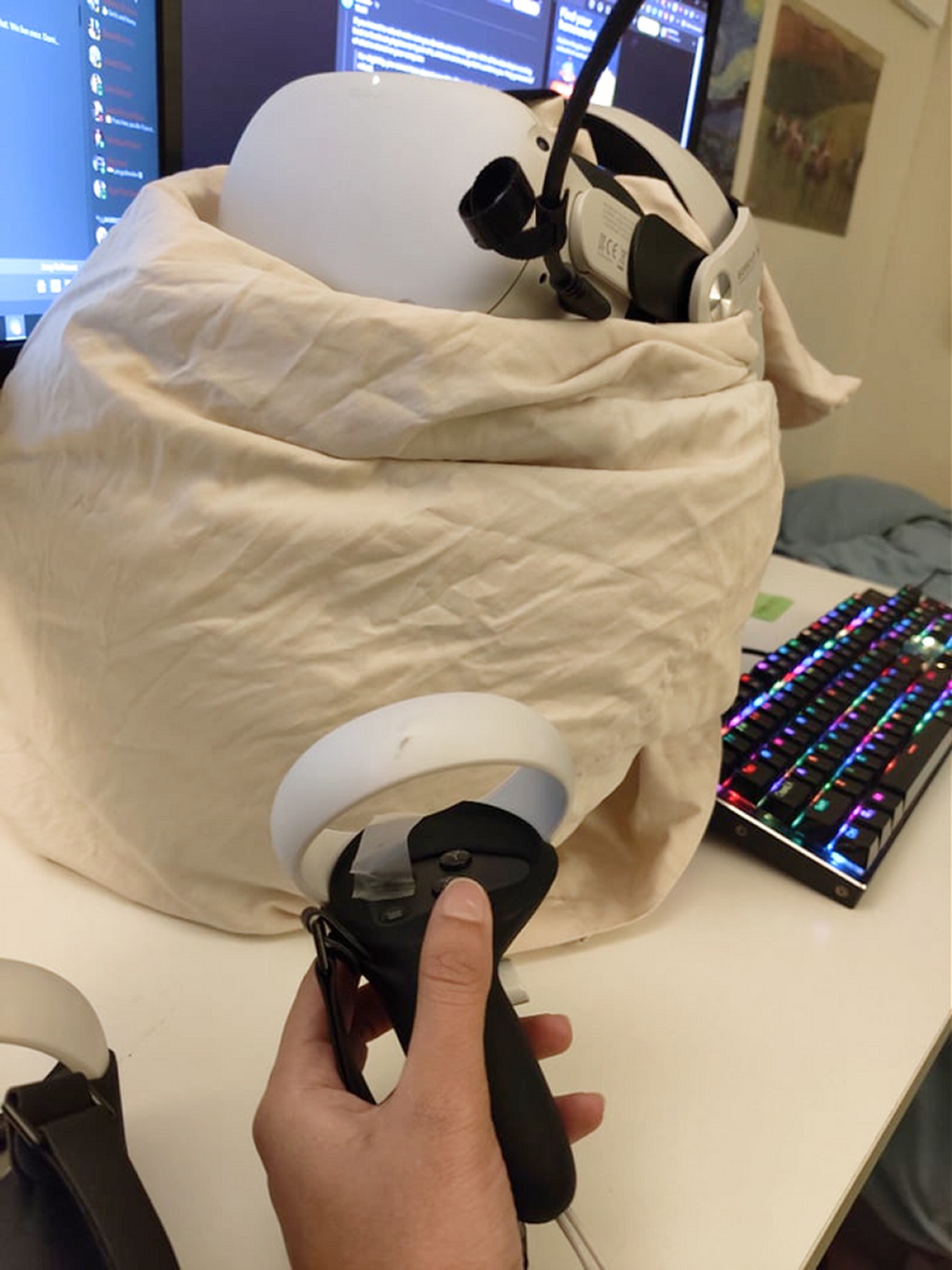 The workaround in real life: an Oculus Quest 2 headset stuffed into a pillow to keep its proximity sensor covered, running on a desk beside a keyboard